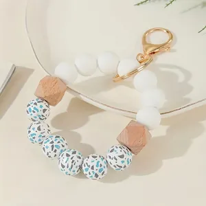 Silicone and wooden bead keychain with gold lobster clasp on white ceramic tray