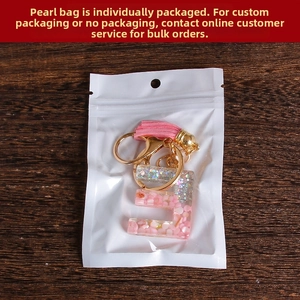 Detail of pink resin letter E keychain with glitter flakes and leather tassel in packaging