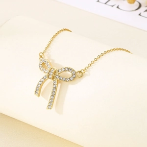 Polished gold stainless steel bow necklace with sparkling zircon pavé on beige background
