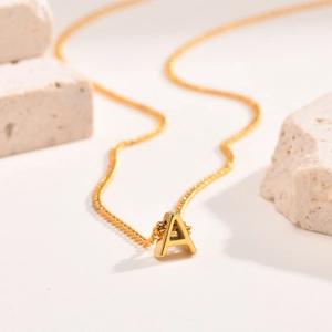 Close-up of polished gold A-letter pendant on delicate stainless steel chain on stone