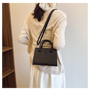 Rear view of a model wearing a black square crossbody bag with dual handles in a home setting