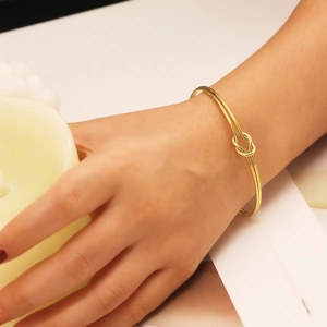 Detailed view of an 18k gold plated stainless steel knot bracelet worn on a wrist