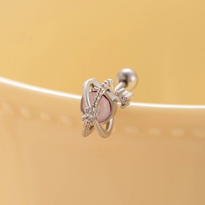 Saturn shaped titanium steel stud earring with pink zircon stone on ceramic background