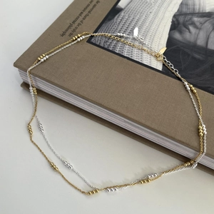 Detail of minimalist 925 silver beaded necklace with mixed gold and silver finish on book