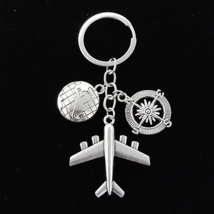 Silver metal travel keychain set with earth, compass, and airplane pendants on black background