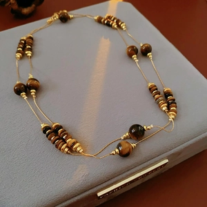 Vue détaillée de perles oeil de tigre marron et disques dorés sur un coffret en velours gris