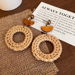 Detail of bohemian round straw woven earrings with wooden accents and gold studs