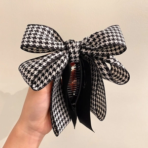 Detail of a black and white houndstooth fabric bow hair clip with a sturdy plastic base