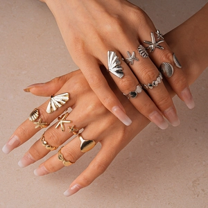 Detail of mixed metal starfish and seashell rings styled on hands for beach vacations