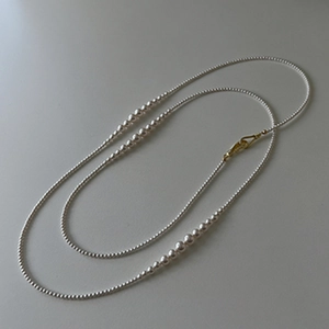 Detail of elegant long pearl necklace with gold J-hook connector and thin bead strands