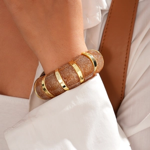 Detail of chunky brown resin bracelet with gold glitter and metallic rings on a model