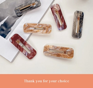 Detail of five acrylic hair clips with marble texture and golden duckbill metal clips