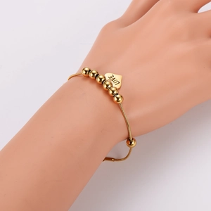 Minimalist gold beaded heart charm bracelet with LOVE engraving shown on wrist