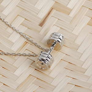 Barbell pendant necklace in silver stainless steel on a rustic woven bamboo background