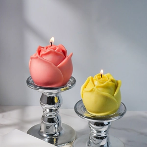 Détail de bougies en forme de rose rose et jaune allumées sur des supports en métal argenté
