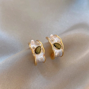 Detail of French luxury hoop earrings with green zircon and wavy textured gold finish