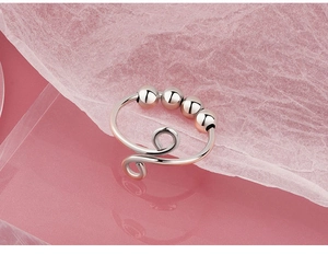 Detail of silver anti-anxiety spinner ring featuring four movable beads on a pink background
