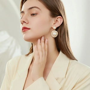 Detail shot of a round gold pearl earring with zircon halo on model in beige blazer