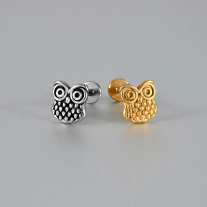 Détail des piercings labret en forme de hibou avec finitions or et argent poli