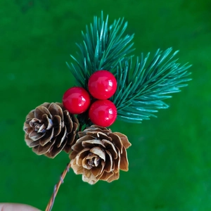 Artificial Christmas branch with natural pine cones, red berries and needles on green background