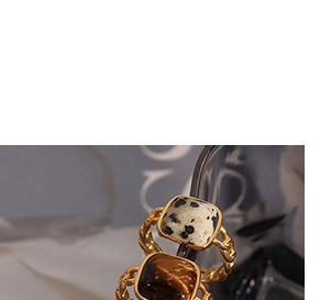 Detail view of gold twisted chain rings featuring square spotted stone and tiger eye gems