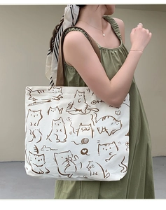 Side view of white canvas tote bag with brown cat print worn by model on shoulder