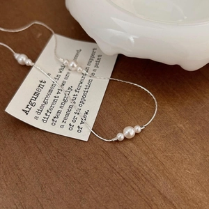 Close-up of minimalist S925 silver necklace with elegant white pearls on a wood surface
