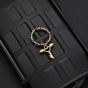 Close-up of beaded ring with colorful crystals and a winged heart key charm on black box