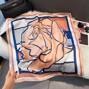 Dettaglio di sciarpa in seta con stampa rosa su tappeto morbido e borsa in pelle nera