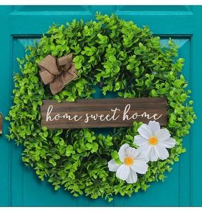Detail of green leaf wreath with wooden home sweet home sign and white daisies on teal door