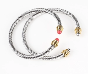 Detailed view of cable wire bangle with gold caps and red beads on white background