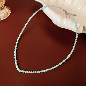 Close-up of light blue amazonite beaded necklace on a white shell plate and brown surface