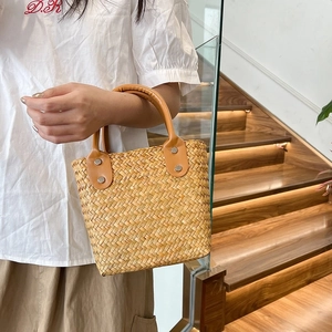 Macro shot of handwoven straw bag featuring caramel leather handles and metal rivets