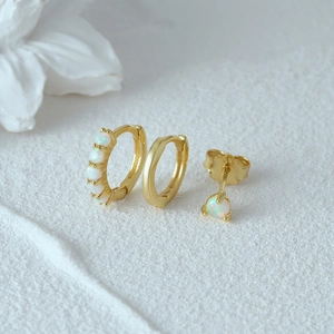 Detailed view of three gold vermeil earrings with white opals on a white floral surface