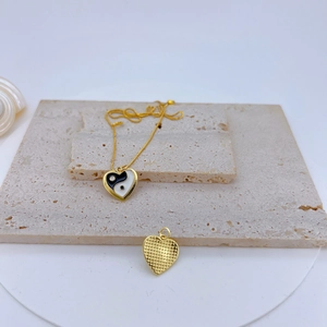 Close-up of gold-plated heart pendant with black and white yin yang inlay on beige stone