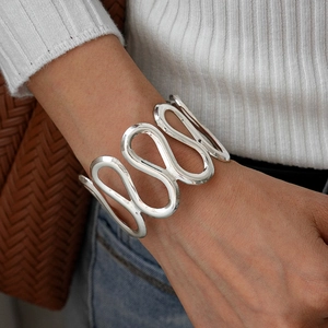 Detailed view of wide silver hollow wavy cuff bracelet worn on wrist for a modern look