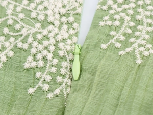 Detailed macro view of white floral embroidery and invisible zipper on green pleated fabric