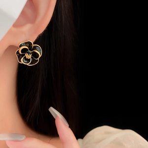 Detail of vintage black camellia earrings with gold trim worn by a model