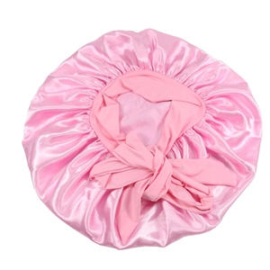 Flat lay of a large pink satin hair bonnet with wide adjustable ribbon ties for hair care