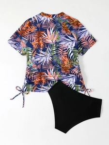 Flat lay of two-piece tankini set with tropical leaf print top and high-waisted black bottom