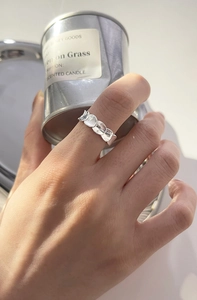 Detalle del anillo de plata con diseño de escamas frente a un frasco de vela metálico