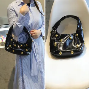 Close-up of black crescent shoulder bag with dense gold metallic rivets on white chair