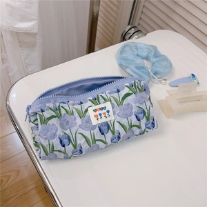 Detail of blue floral fabric pouch with tulip pattern and zipper on white surface
