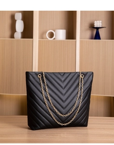 Macro shot of black V-quilted faux leather bucket bag with gold metal chain strap