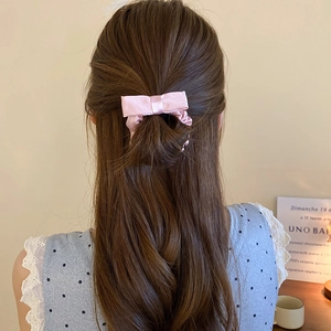 Pink satin bow scrunchie shown on long wavy hair with a soft elegant aesthetic