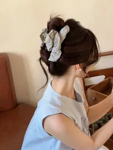 Detailed back view of a woman wearing a light gray pleated fabric claw clip in her hair
