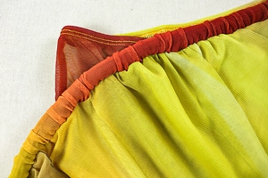 Macro detail of elastic waist and orange-yellow mesh fabric stitching on the dress