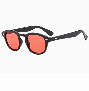 Detail view of retro round sunglasses featuring thick black frames and red tinted lenses