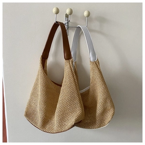 Close-up of woven straw shoulder bags with brown and white leather straps on wall
