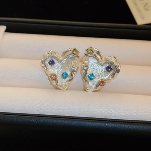Macro shot of silver heart earrings with lava texture and colorful inlaid zircons